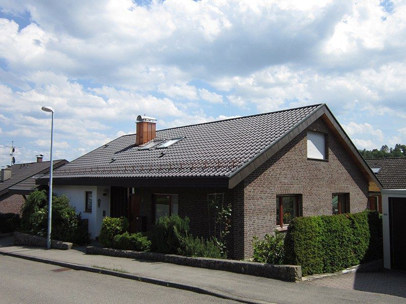 HB Holzbau Breymaier GmbH – Wohnhaus aus Stein mit stilvoller Bedachung in dunklen Farbtönen