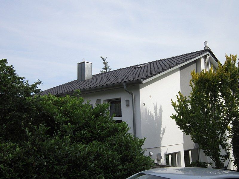 HB Holzbau Breymaier GmbH – Blick auf Wohnhaus hinter Bäumen, neues Schrägdach nach Fertigstellung