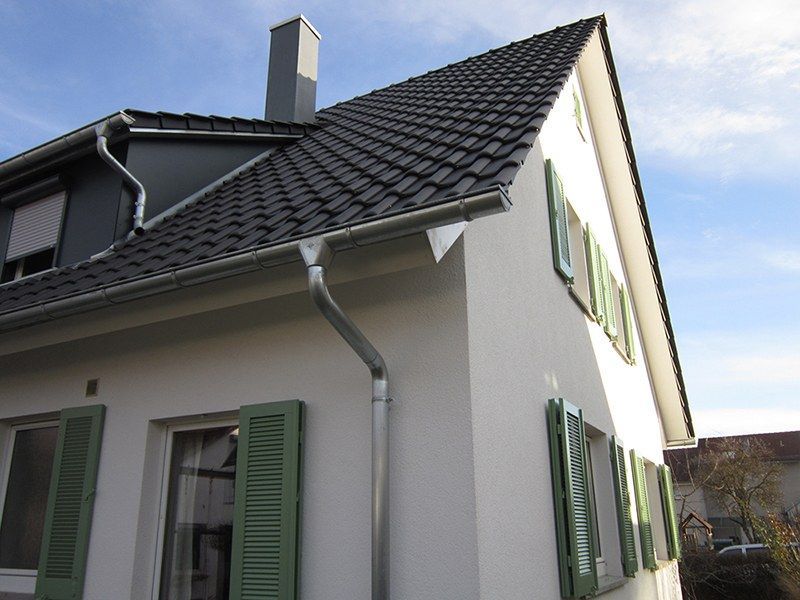 HB Holzbau Breymaier GmbH – 
Sicht auf eine weiße Hausfassade mit neuem Schrägdach und glänzender Regenrinne