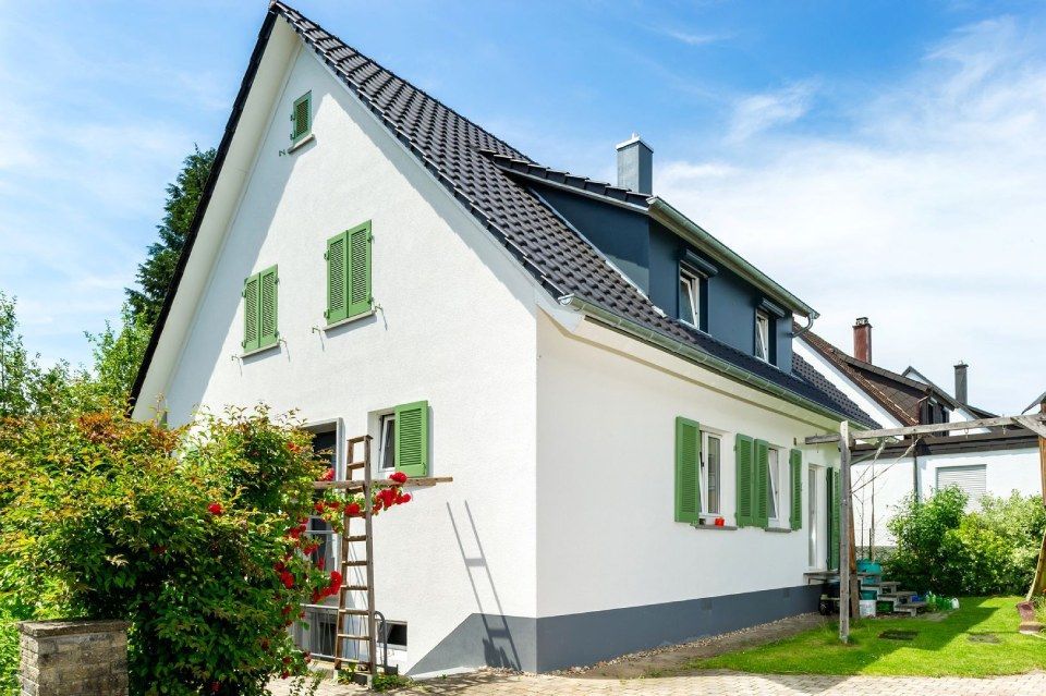 HB Holzbau Breymaier GmbH – weißes Wohnhaus mit grünen Fensterläden und schwarzem Schrägdach