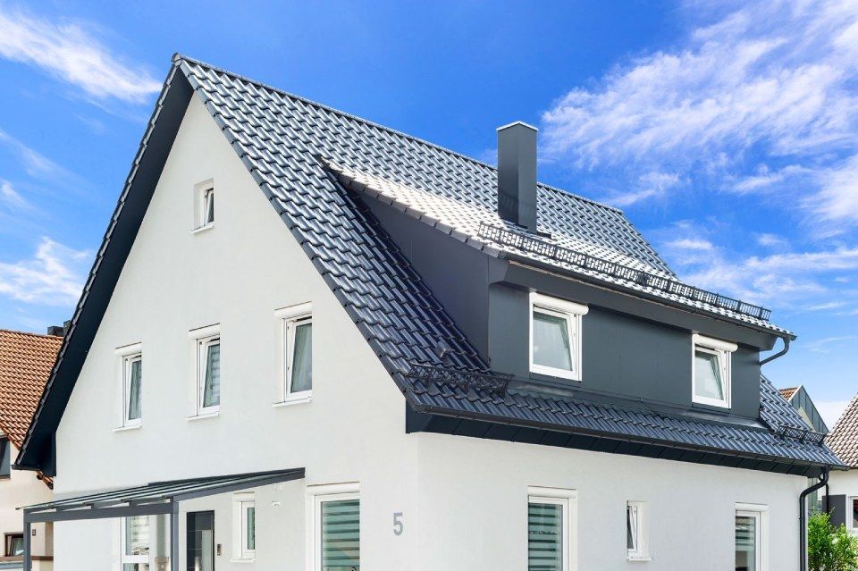HB Holzbau Breymaier GmbH – kontrastreiches Foto eines weißen Mehrfamilienhauses mit schwarzen Dachschindeln vor blauem Himmel