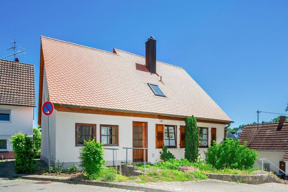 HB Holzbau Breymaier GmbH – kontrastreiches Foto eines weißen Mehrfamilienhauses mit orangen Dachschindeln vor blauem Himmel