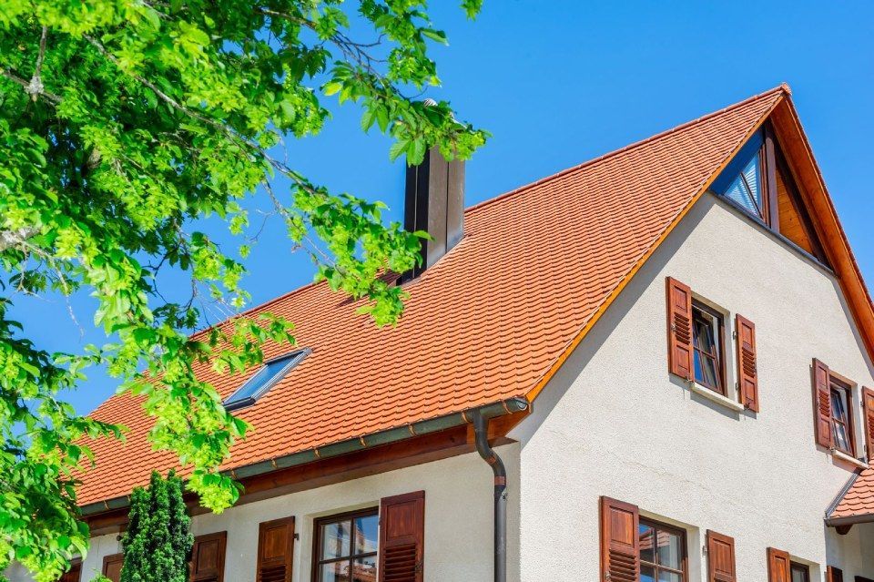 HB Holzbau Breymaier GmbH – kontrastreiches Foto eines weißen Mehrfamilienhauses mit orangen Dachschindeln vor blauem Himmel