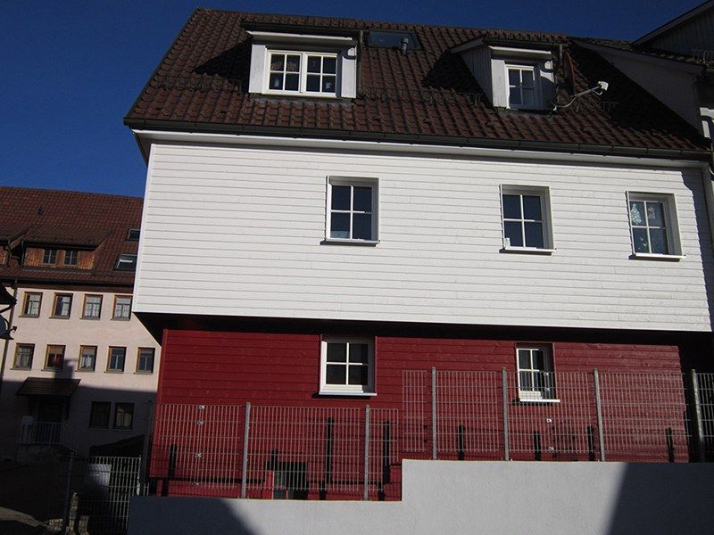 HB Holzbau Breymaier GmbH – Hausfassade mit rötlicher Holzvertäfelung im Erdgeschoss und weißer Vertäfelung im ersten Stock