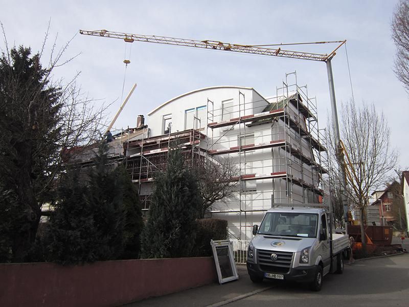 HB Holzbau Breymaier GmbH – Ein Kran neben einem weißen mehrstöckigen Gebäude mit Baugerüsten