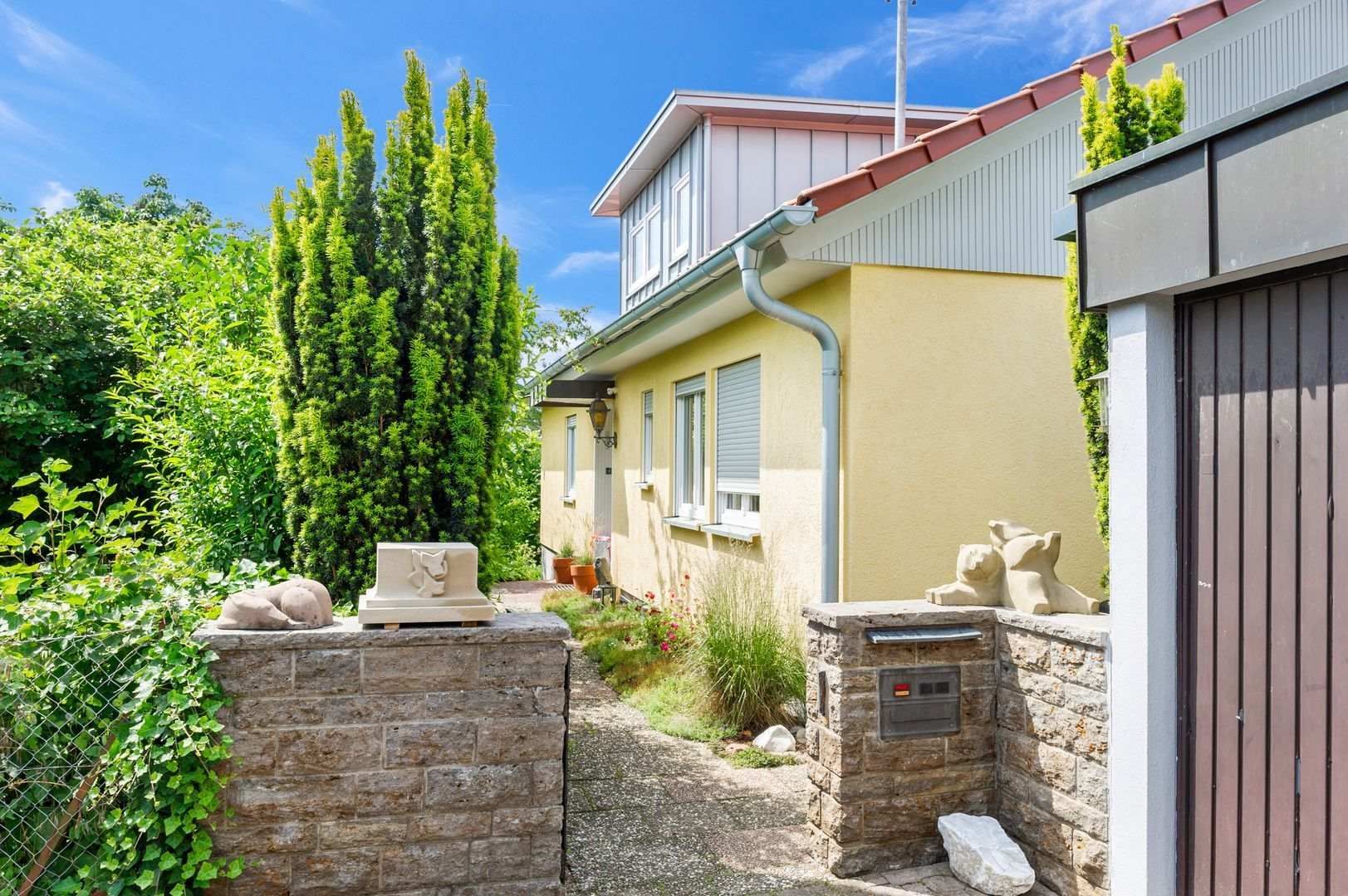 HB Holzbau Breymaier GmbH – Sicht auf gelbes Gebäude mit Steinmauer im Vordergrund