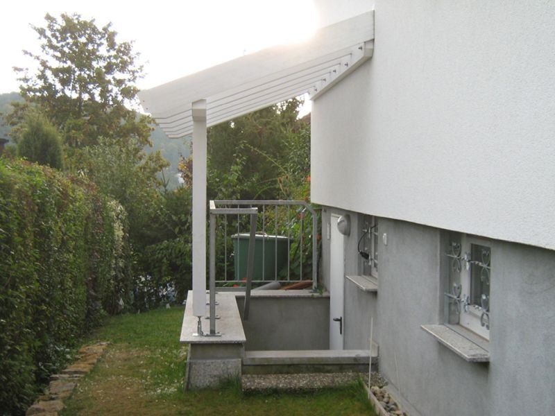 HB Holzbau Breymaier GmbH – Kellereingang an einer Hausfassade mit dekorativem Vordach als Wetterschutz