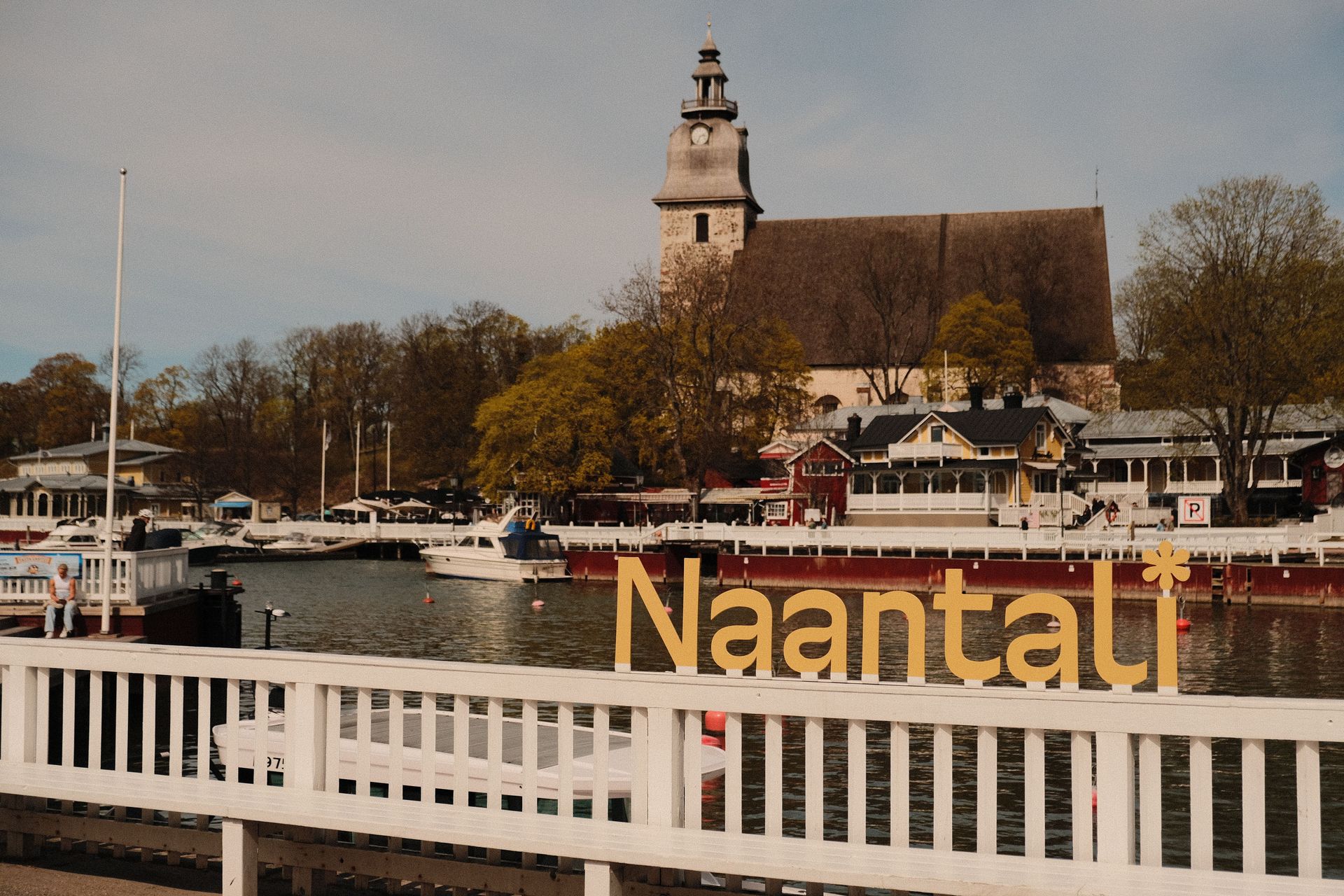 Harbor view of Naantali with a church tower, boats, and a white railing in the foreground