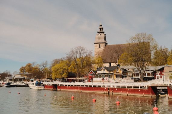Harbor with red boats, riverside buildings, and a tall tower under autumn trees at dusk