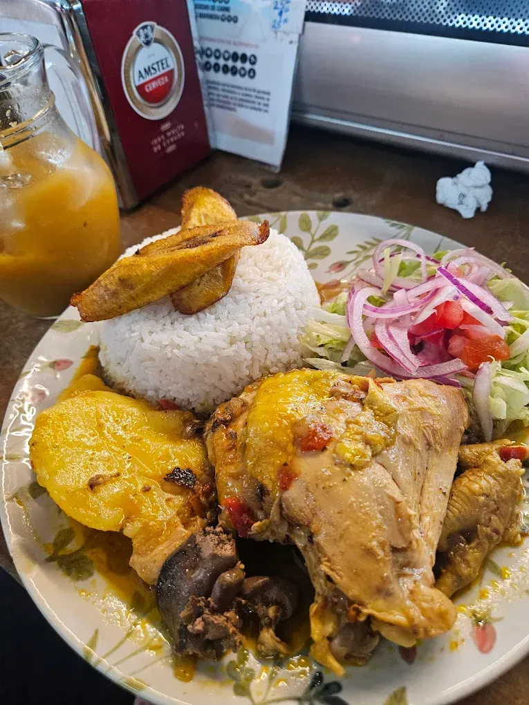 Un plato con arroz blanco, plátanos fritos, pollo guisado con patatas amarillas y una ensalada con cebolla roja.
