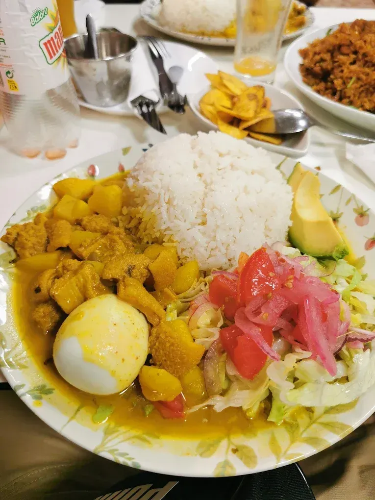 Un plato de curry con huevo duro, arroz blanco, ensalada con cebollas encurtidas y aguacate, con guarniciones a la vista.