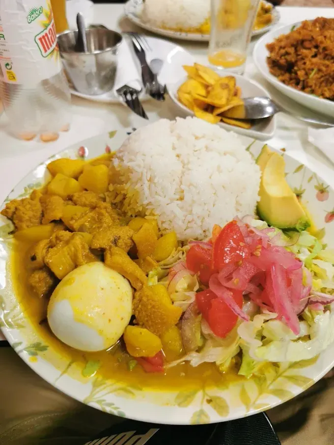 Un plato de curry con huevo duro, arroz blanco, ensalada con cebollas encurtidas y aguacate, con guarniciones a la vista.