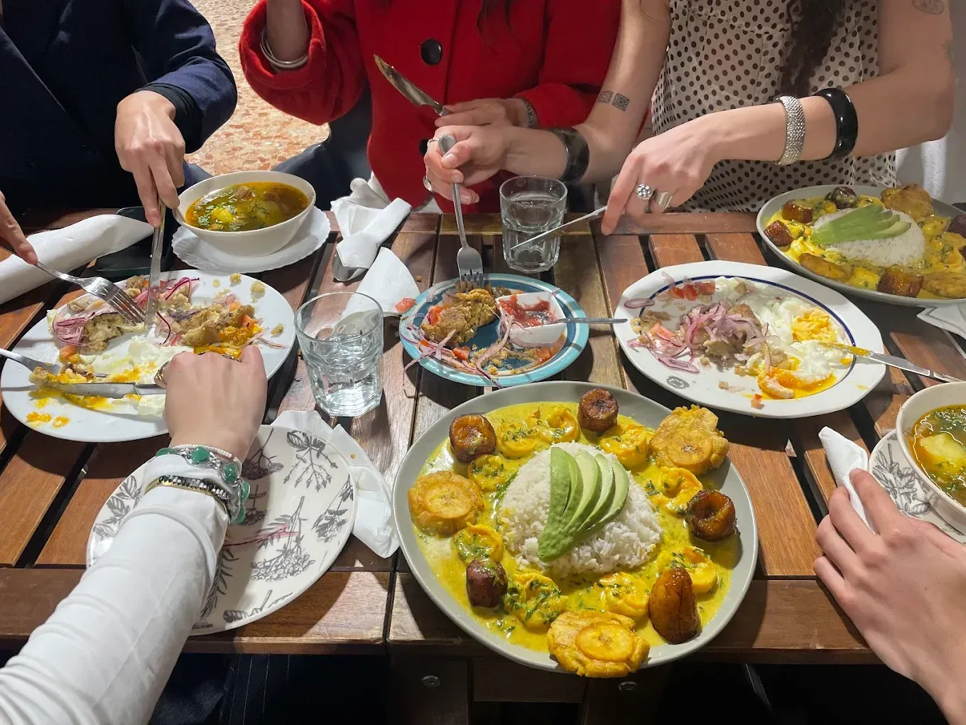 Varias personas disfrutan de una comida que consiste en platos de arroz, aguacate y plátanos en una mesa de madera.