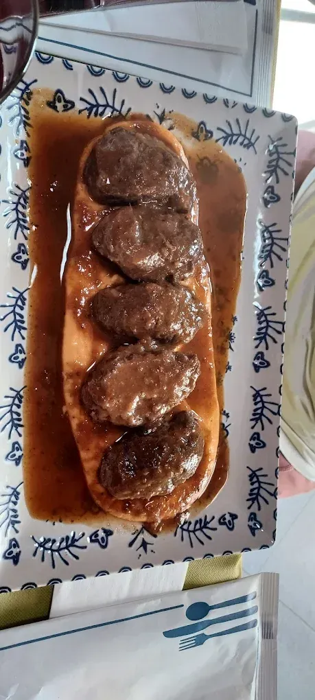 Un plato rectangular con una hogaza de pan, cubierto con hamburguesas y salsa marrón.