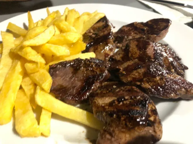 Hígado a la parrilla con patatas fritas en un plato blanco.