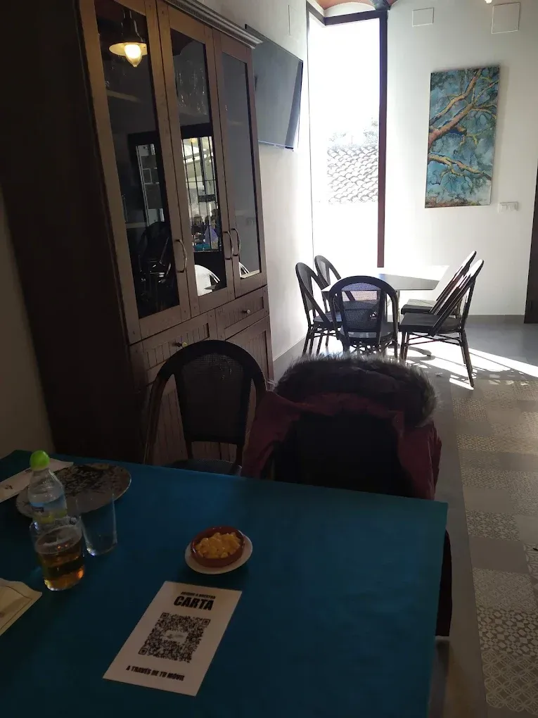 Comedor interior: una mesa azul con comida/bebidas en primer plano; un juego de comedor al fondo; un mueble armario.