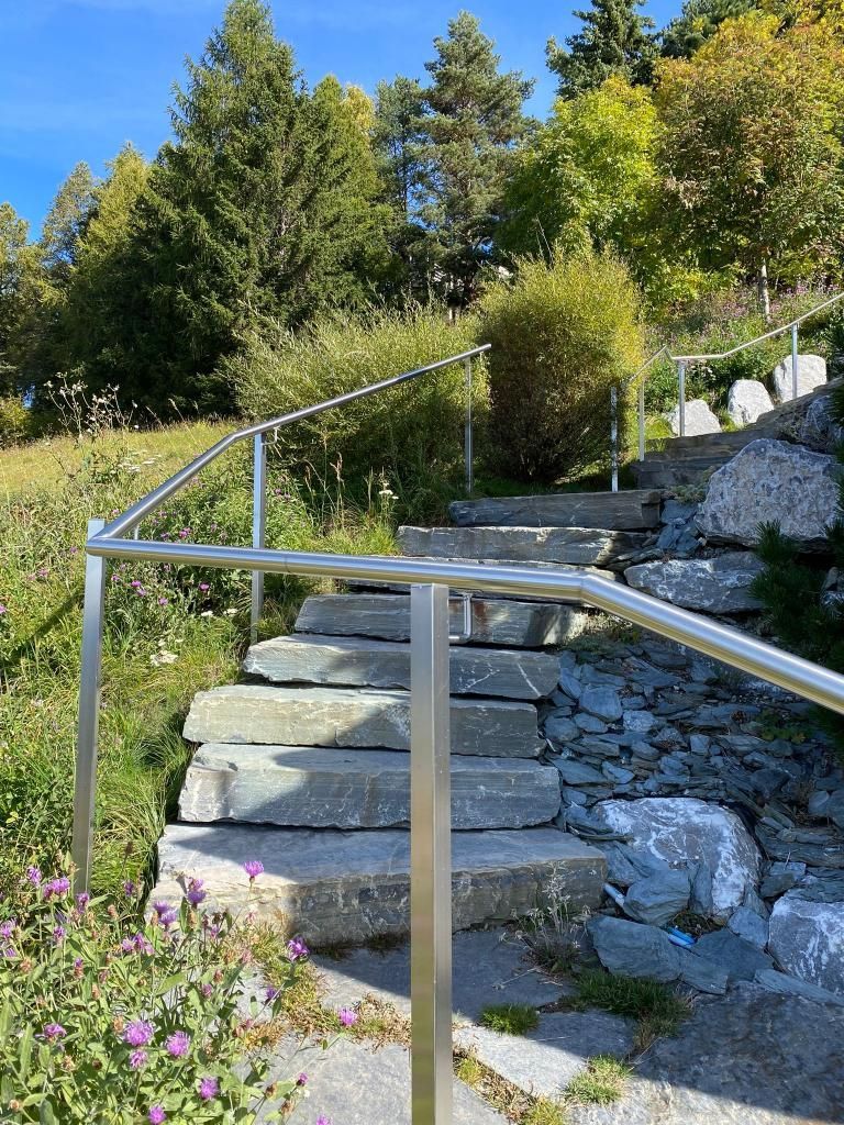 Un escalier avec une rampe en acier inoxydable menant à une colline.