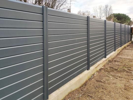 Une clôture grise se trouve au sommet d'un champ de terre.