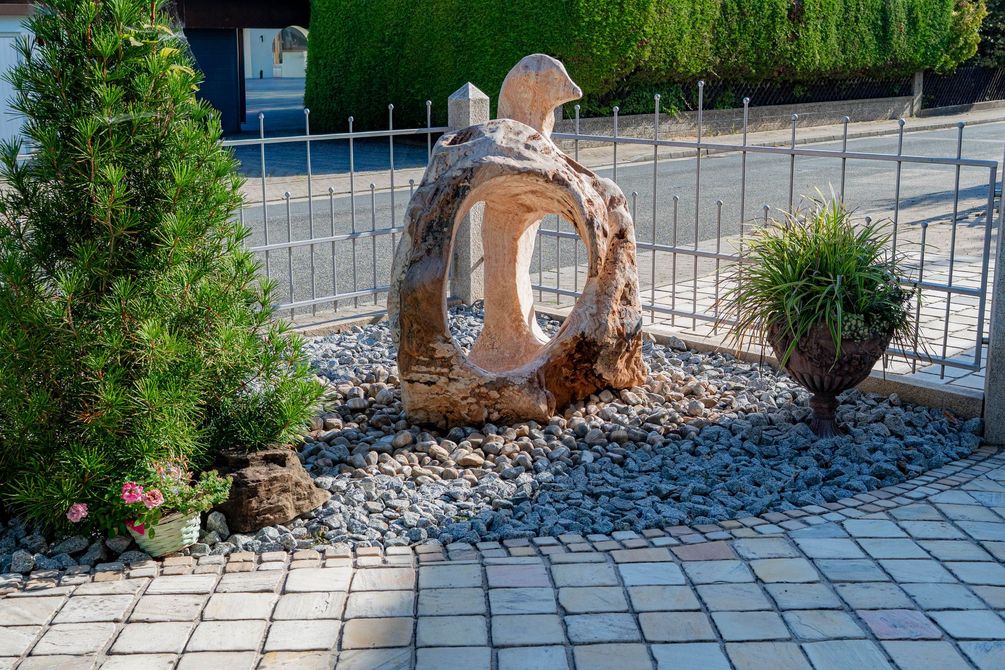 Modern bepflanzter Vorgarten mit kleinen Tannen, Tonkrügen und einer Stein/Holz-Skulptur