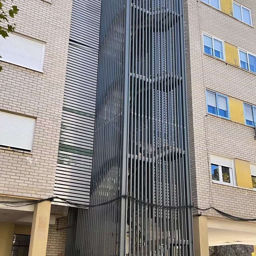 Edificio exterior con escalera metálica con reja. Edificio de ladrillo beige con marcos de ventanas amarillos.