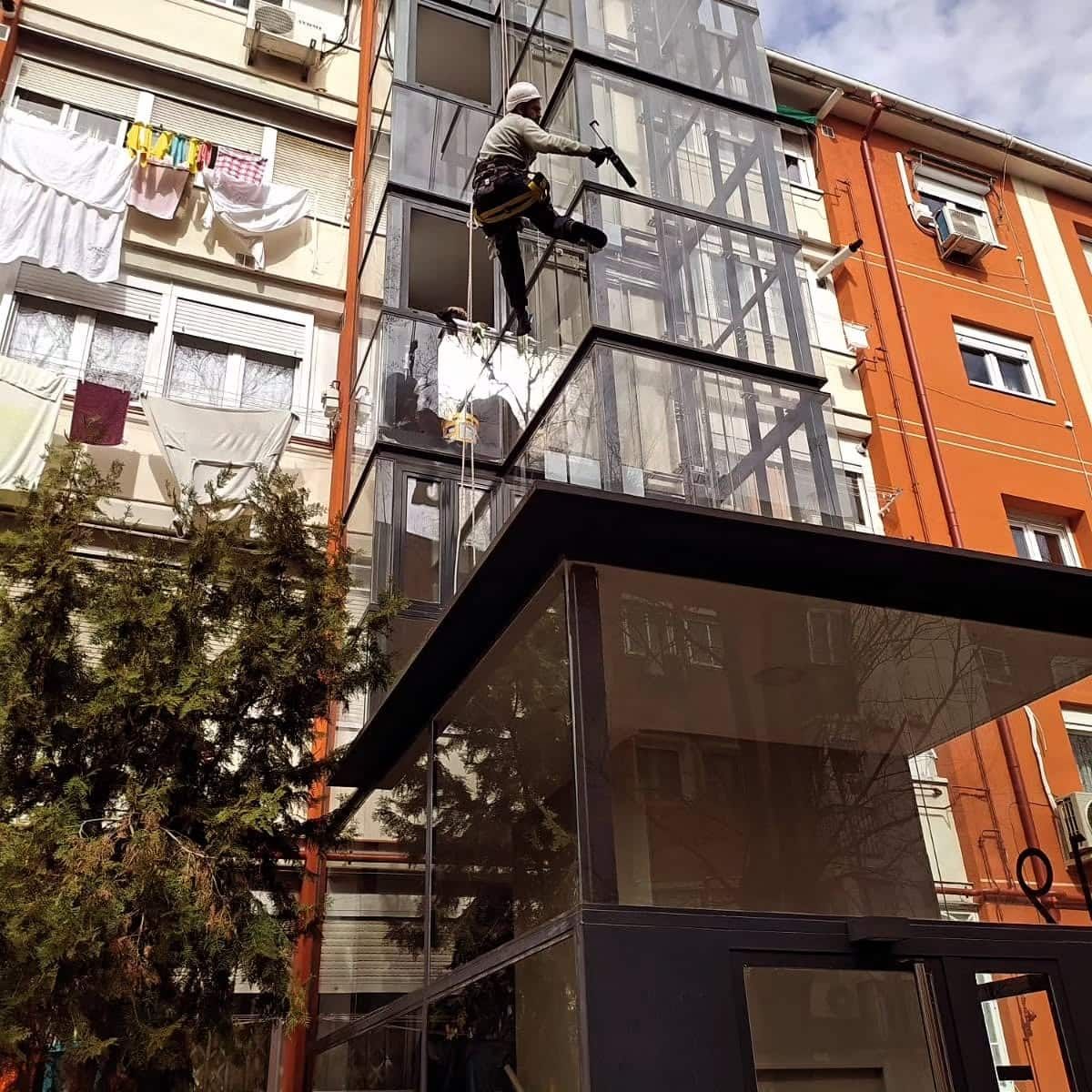Trabajador en un andamio, limpiando un ascensor transparente afuera de un edificio de apartamentos.