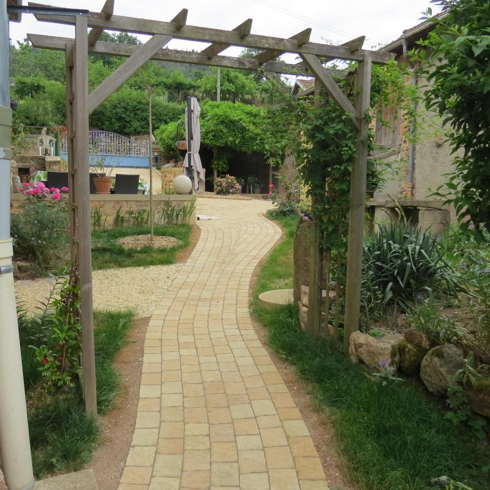 Un chemin de briques sinueux traverse un jardin luxuriant sous une pergola en bois
