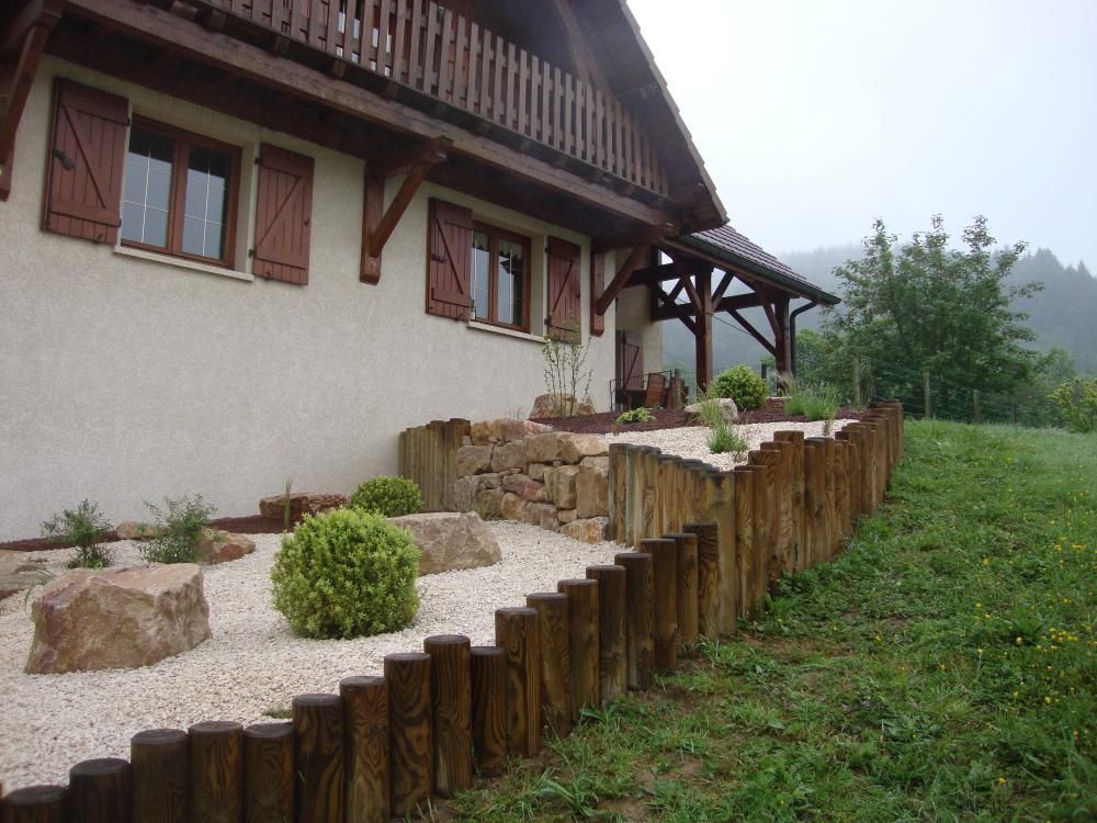 Maison avec balcon en bois et terrasse de jardin en pierre, au bord d’une pente herbeuse