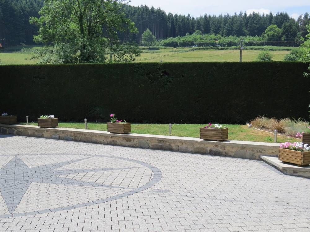 Cour intérieure pavée avec des jardinières donnant sur un champ verdoyant et une forêt au-delà d’une haie sombre.