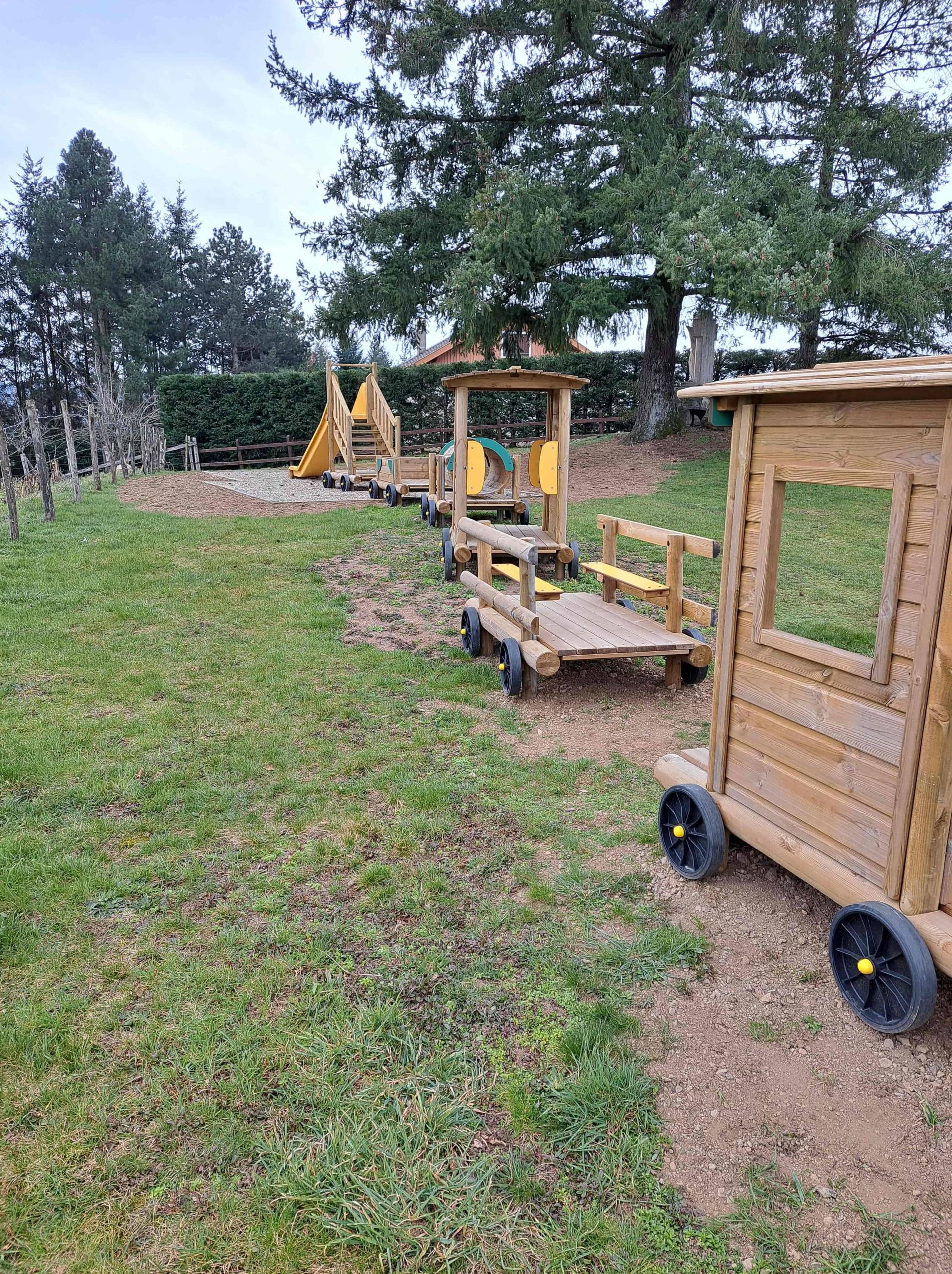 Train et wagons en bois sur un chemin herbeux, à côté d’une clôture de jardin et d’arbres