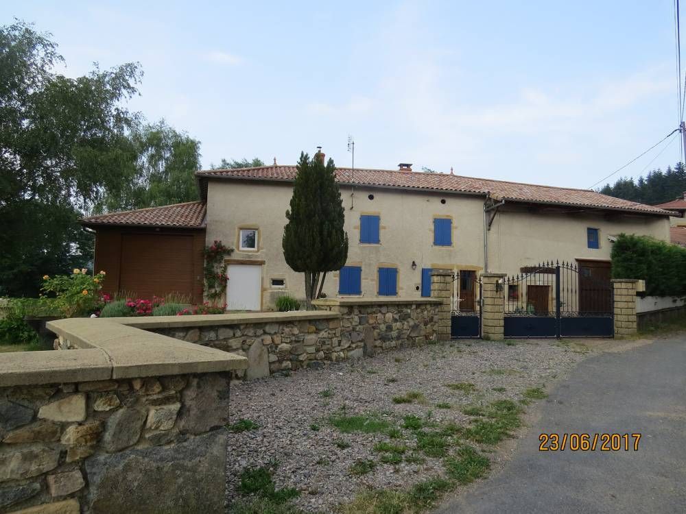 Maison de campagne en pierre aux volets bleus, avec une cour gravillonnée, vue depuis la rue.