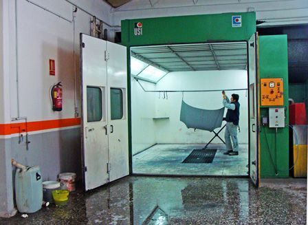 Una persona cuelga un gran panel de tela gris en una zona de lavado industrial verde con el suelo mojado.