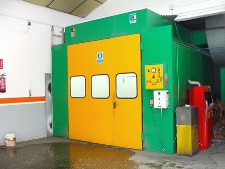 Máquina industrial verde con puertas amarillas y panel de control en una sala de la fábrica.