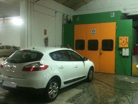 Coche blanco en un área de lavado de coches con puertas naranjas y verdes bajo luces brillantes