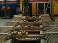 Sistema de transporte de fábrica con rodillos metálicos y maquinaria roja en un entorno industrial.
