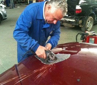 Mecánico puliendo el capó de un coche color granate con una pulidora en un garaje.