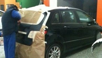 Persona cubriendo un coche negro con papel protector en un taller.
