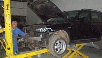 SUV negro en un elevador en un taller mecánico mientras un mecánico trabaja en la parte delantera.