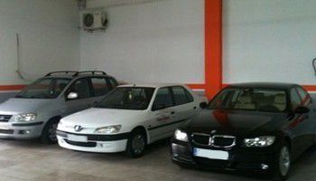 Tres coches aparcados en un garaje, entre ellos sedanes plateados, blancos y negros.