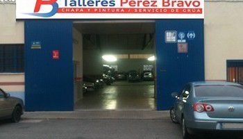 Entrada de taller mecánico con puertas azules abiertas y coches aparcados fuera.