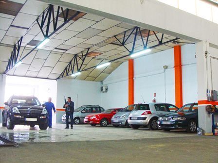 Sala de exposición interior de un concesionario de automóviles con varios coches aparcados y dos personas de pie dentro.