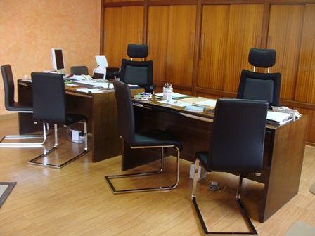 Sala de conferencias con paneles de madera, una mesa larga y varias sillas de oficina negras.