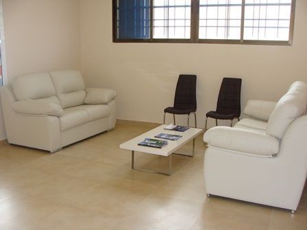 Sala de estar minimalista con dos sofás blancos, dos sillas negras y una mesa de centro baja junto a la ventana.