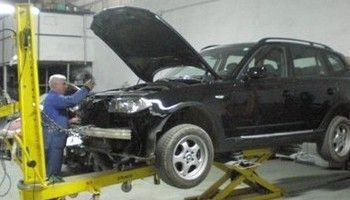 Mecánico inspecciona un SUV negro en un elevador con el capó abierto en un taller de reparación de automóviles.