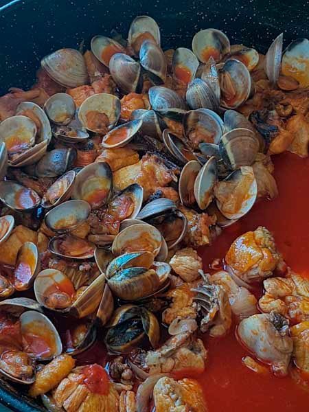 Una sartén llena de almejas y pollo en salsa.