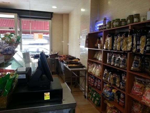 El interior de una tienda de comestibles con una caja registradora y estantes llenos de comida.
