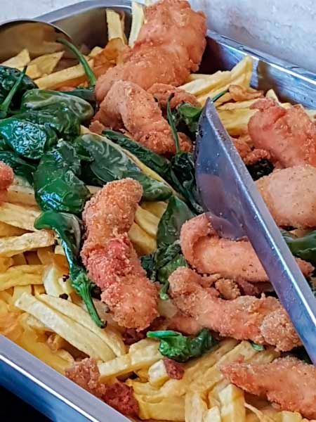 Una bandeja de pollo frito y papas fritas con pinzas.