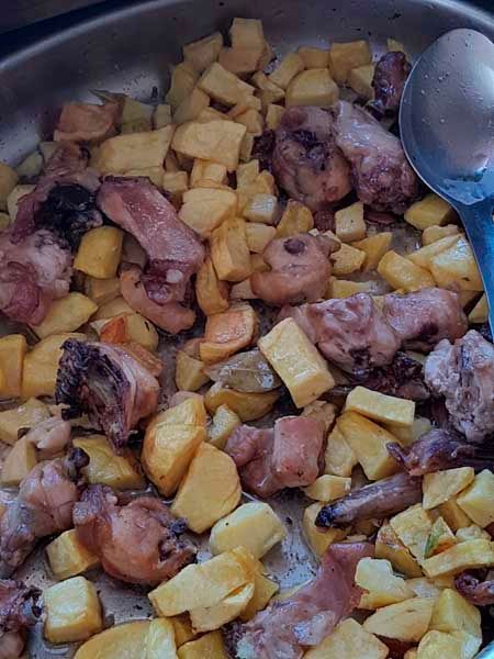 Una sartén llena de carne y patatas con una cuchara dentro.