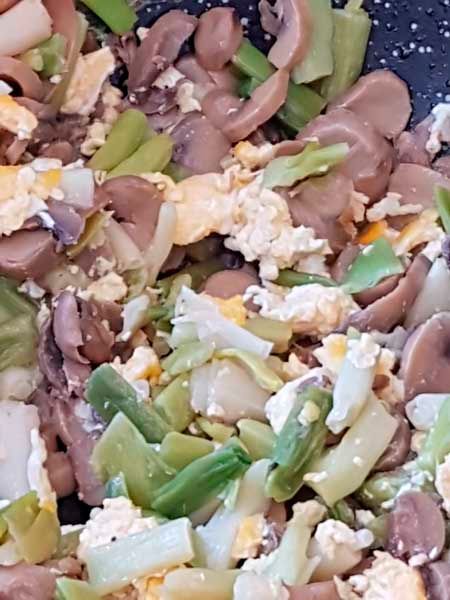 Un primer plano de un salteado con champiñones, huevos y cebollas verdes.