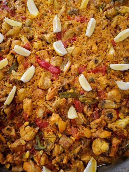 Una cazuela grande llena de arroz, carne, verduras y rodajas de limón.