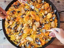 Una persona sostiene un tenedor sobre una sartén de paella.